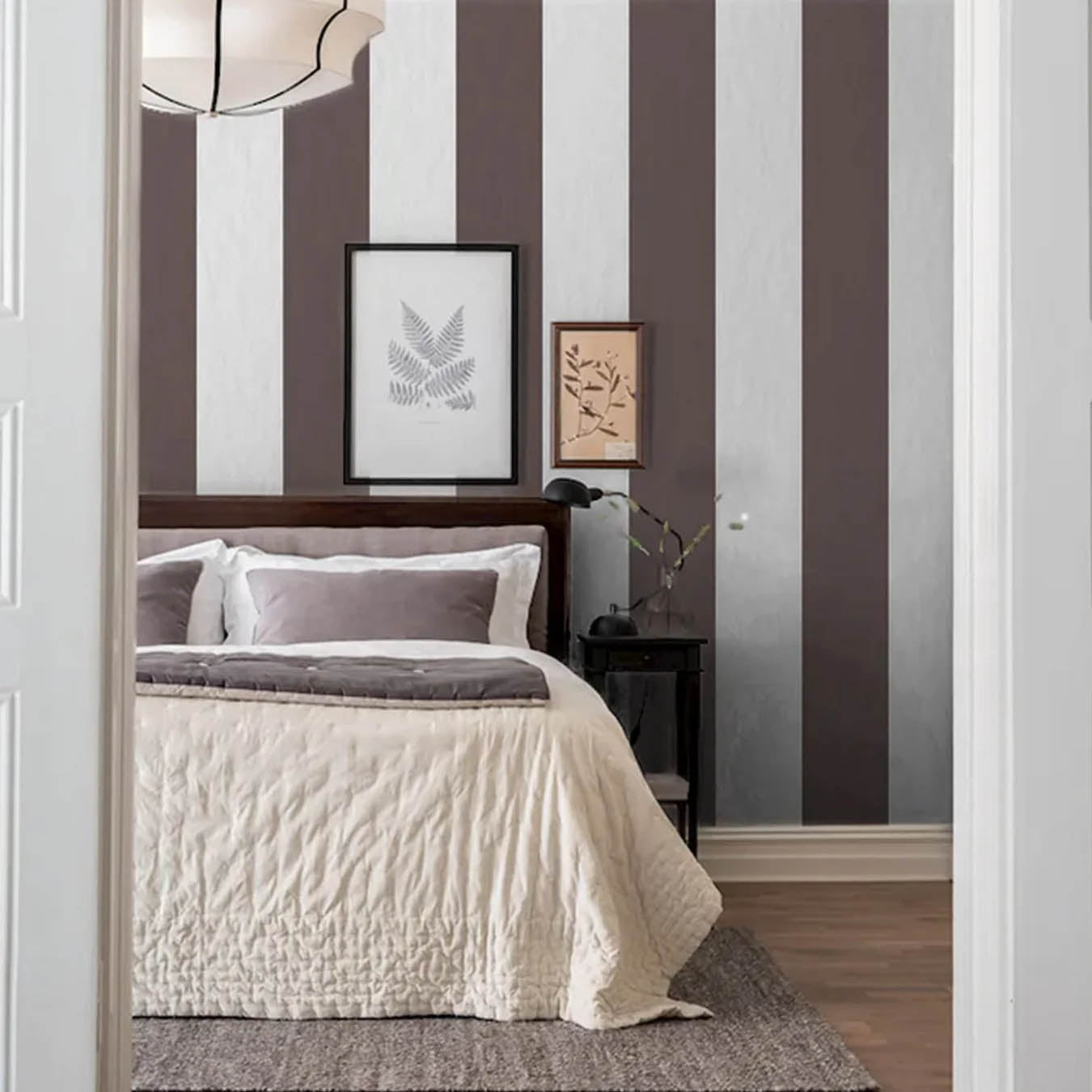 Sovrum med bred randig tapet i brunt och vitt – klassisk och elegant känsla med vit sängkläder och taklampа.